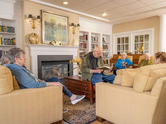 A group of seniors gathered in the living room reading and chatting.