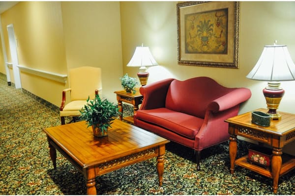 A comfortable seating area with a red couch, a yellow chair, and side tables under warm lighting.
