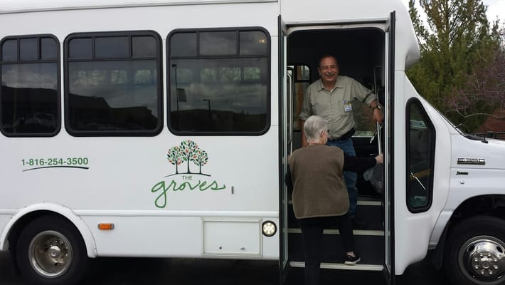 An elderly resident boarding a shuttle bus with the Groves logo.