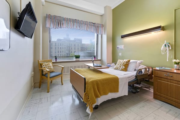 A brightly lit resident room with hospital bed and armchair