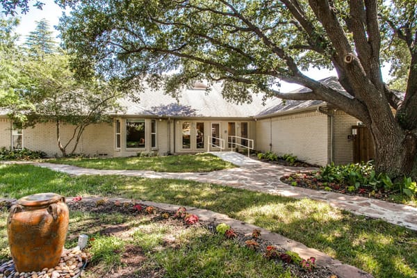 Exterior view of The Sage Oak of Preston Hollow entrance surrounded by green lawn and trees