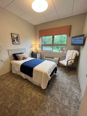 A well-decorated bedroom with a bed, chair, and window showcasing greenery outside.
