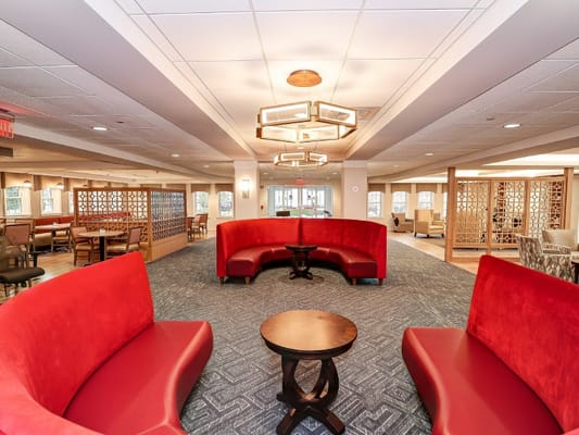 Lounge area with red seating and wooden tables in a senior living facility