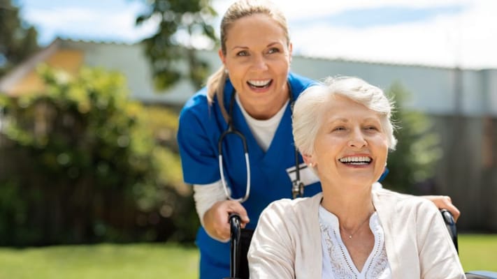A caregiver smiling with a resident in a wheelchair outdoors
