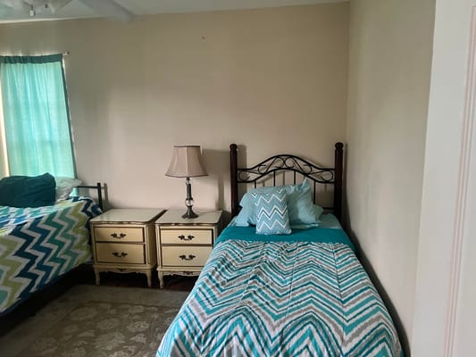 A cozy bedroom with two beds, a lamp, and green curtains.