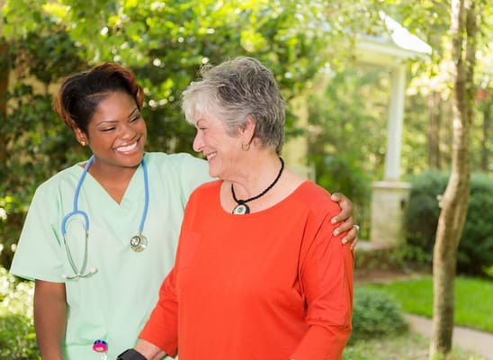 A caregiver and a senior woman smiling at each other outdoors.