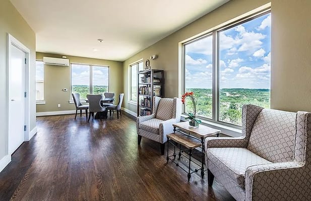 Bright living room with two chairs and dining table, featuring large windows with a scenic view.