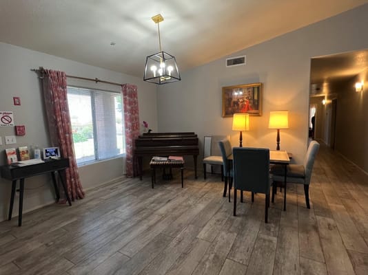 Living room with piano, table, and chairs in a senior living facility.