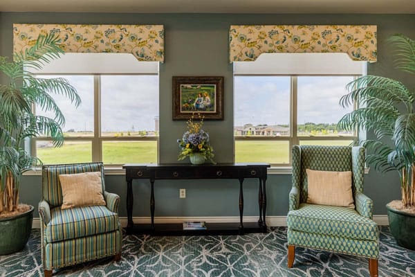 Bright living room with two chairs, decorative plants, and a painting.
