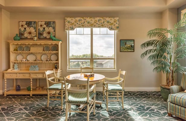 Cozy dining area with a wooden table, chairs, and decorative shelves in a sunlit room.