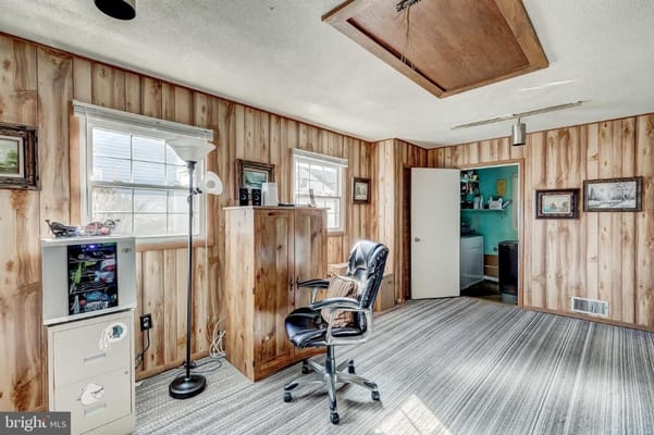 A cozy living room featuring wooden paneling, a chair, lamp, and storage cabinet.