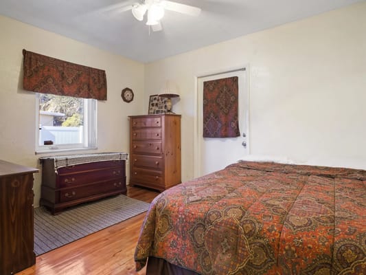 A cozy bedroom featuring a wooden dresser, bed with a colorful quilt, and window.