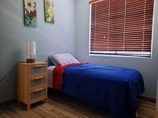 A cozy bedroom with a blue bedspread, nightstand, and window blinds.