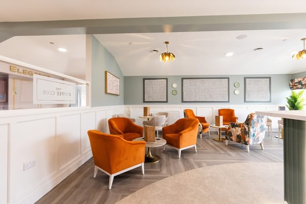 Cozy seating area in the Coffee Club with orange chairs and decorative wall art