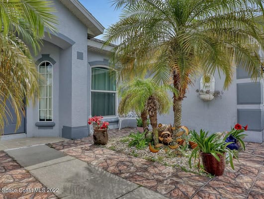 A beautifully landscaped entrance garden featuring palm trees and colorful plants.