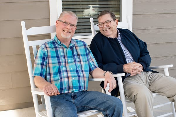 Two male residents sitting on rocking chairs, smiling at the camera.
