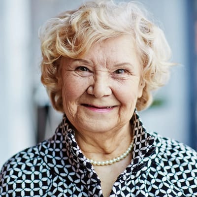 Smiling elderly woman with curly hair in a patterned blouse