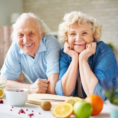 Two smiling senior residents enjoying a kitchen setting with fruits