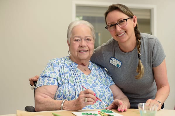 Resident painting with staff assistance in an activity room