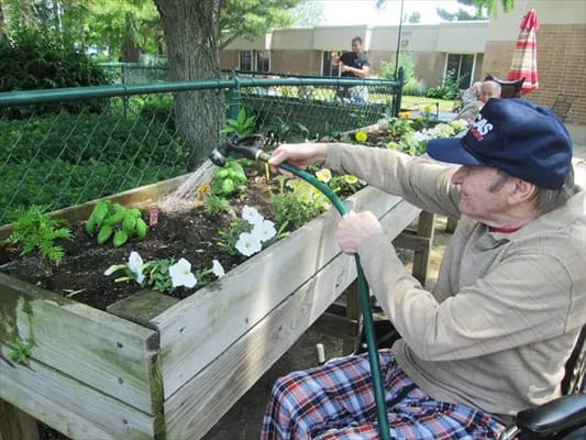 Resident watering flowers in a garden area