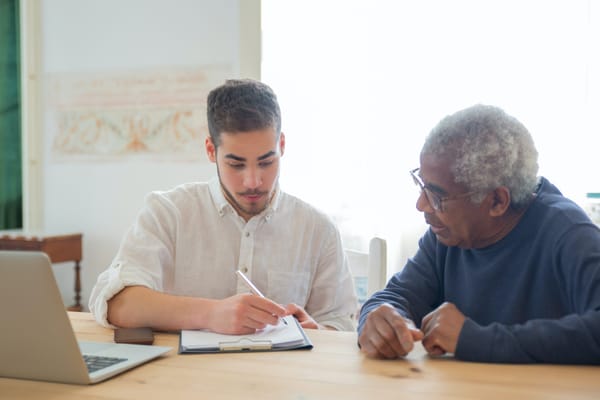 A caregiver assisting an elderly man at a table