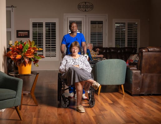 Woman in wheelchair accompanied by staff in a cozy common area