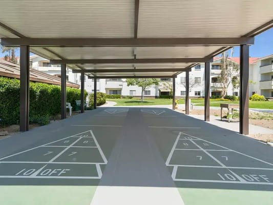 A shaded outdoor shuffleboard court with nearby buildings