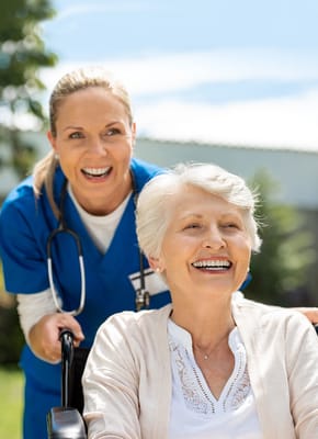 A caregiver and a smiling resident outdoors in a wheelchair