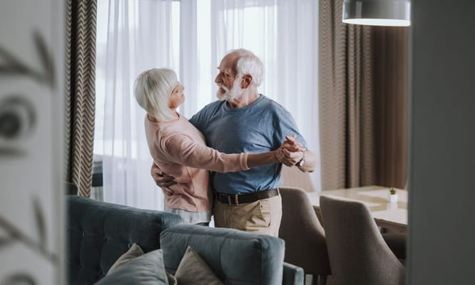 An elderly couple dancing in a cozy living area