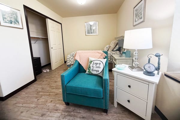 A cozy resident room featuring a teal chair and nightstand