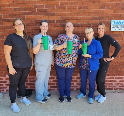 Group of staff members holding green tumblers in front of a brick wall.