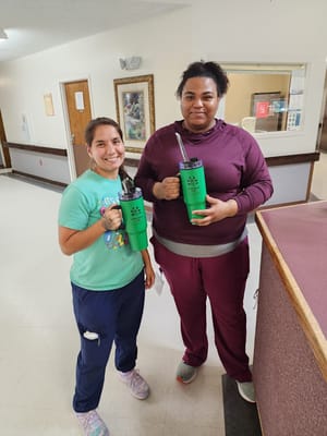 Two staff members holding green water bottles in a hallway.