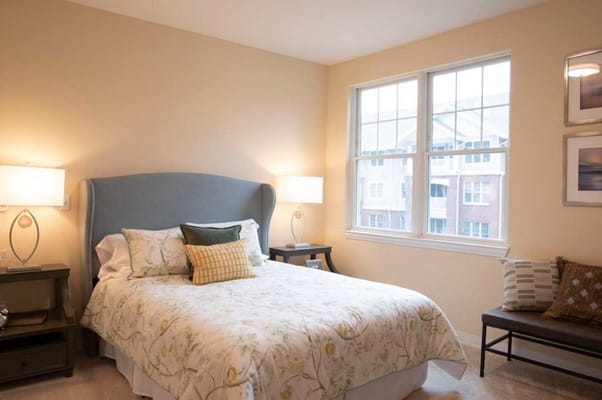 Brightly lit bedroom with a bed, two lamps, and large windows