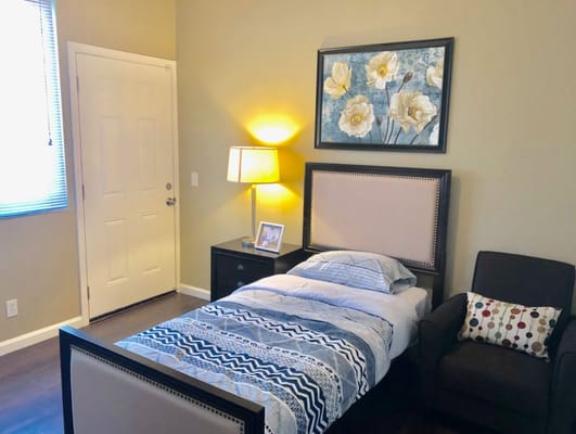 A well-decorated bedroom with a bed, chair, lamp, and art on the wall.