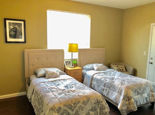 A view of two twin beds in a cozy room with a nightstand and lamp.