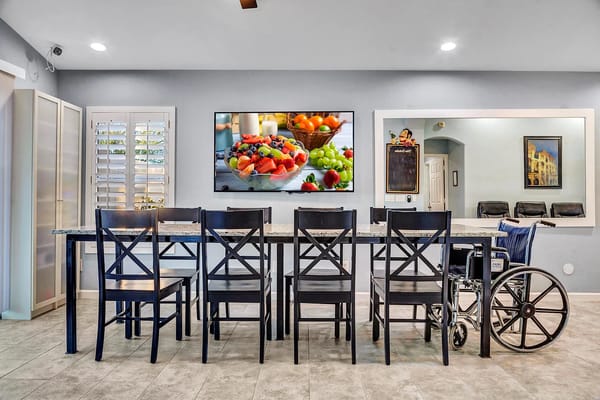 A bright kitchen with a dining table and a television showing a fruit bowl