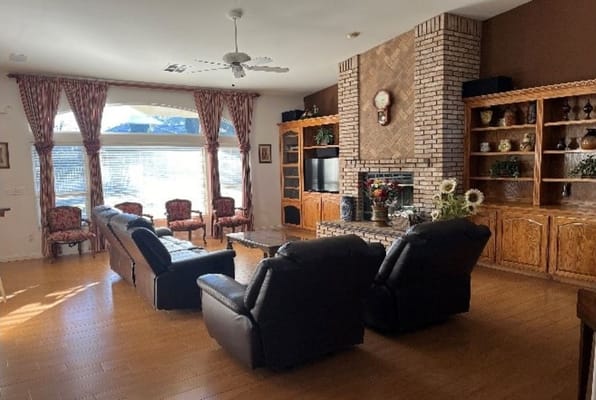 Spacious living room with leather couches, floral curtains, and a brick fireplace.