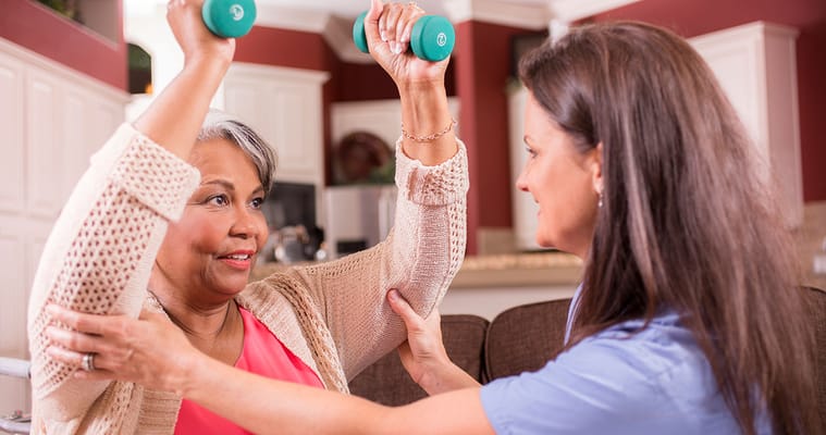 Staff assisting resident with weights during exercise.