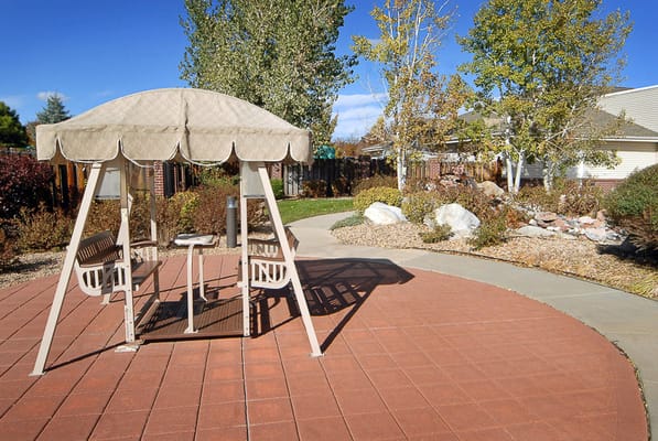 A garden swing with a shaded canopy in a landscaped outdoor area.