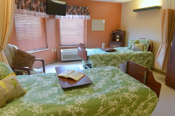 A well-furnished bedroom with two beds, green floral bedding, and a reading table.