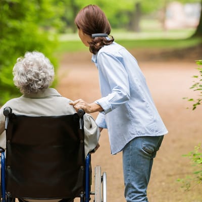 A caregiver pushing a resident in a wheelchair along a serene park pathway.