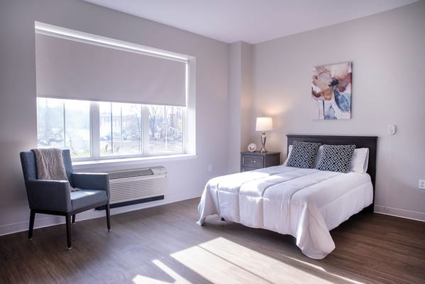 Brightly lit private resident room with a bed and chair