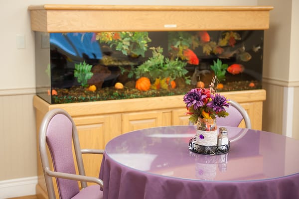 A dining table with a flower arrangement next to a large fish tank.