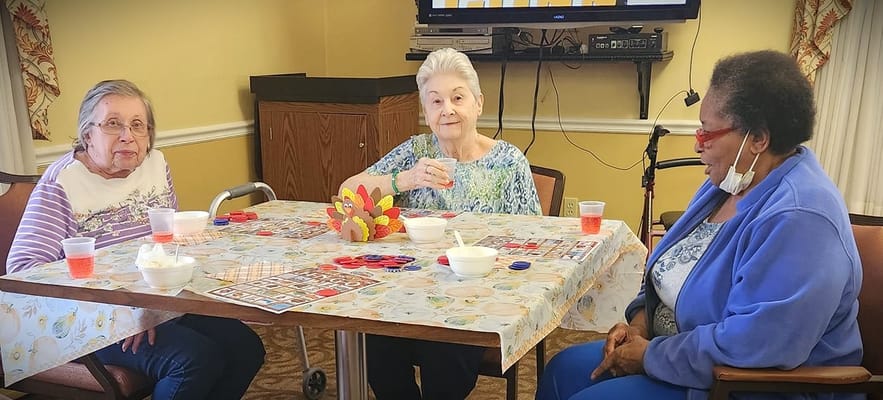 Three senior women playing a game at a table with snacks and drinks.