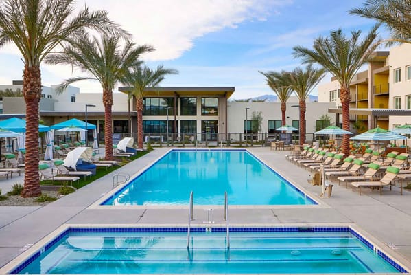 Bright outdoor pool surrounded by palm trees and lounge chairs.