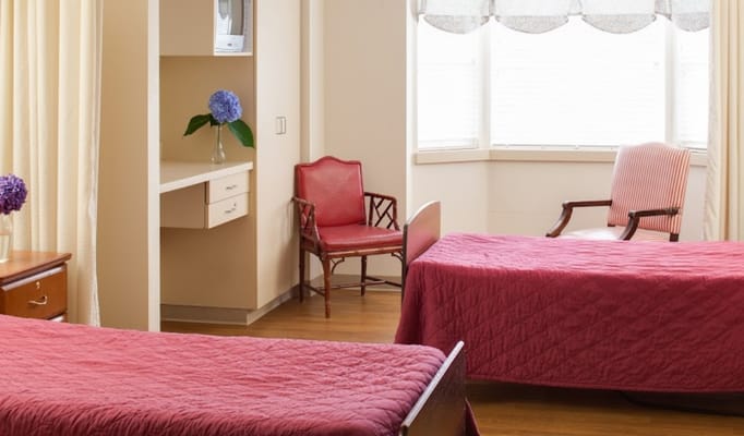 A bedroom with two beds, a chair, and a desk with a vase of flowers.