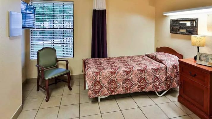 Cozy private room with a bed, chair, and window.