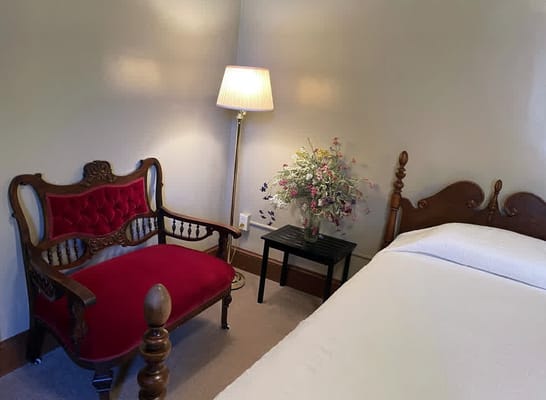 A cozy bedroom featuring a red upholstered chair, a lamp, and a flower vase