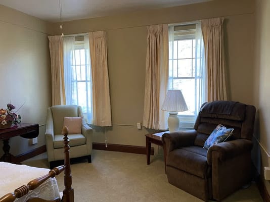 A cozy living room with a light green armchair and a brown recliner beside a table with a lamp.