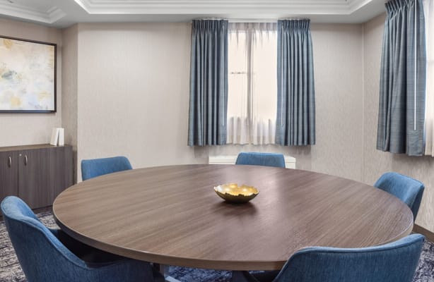 A round wooden table with blue chairs in a conference room.